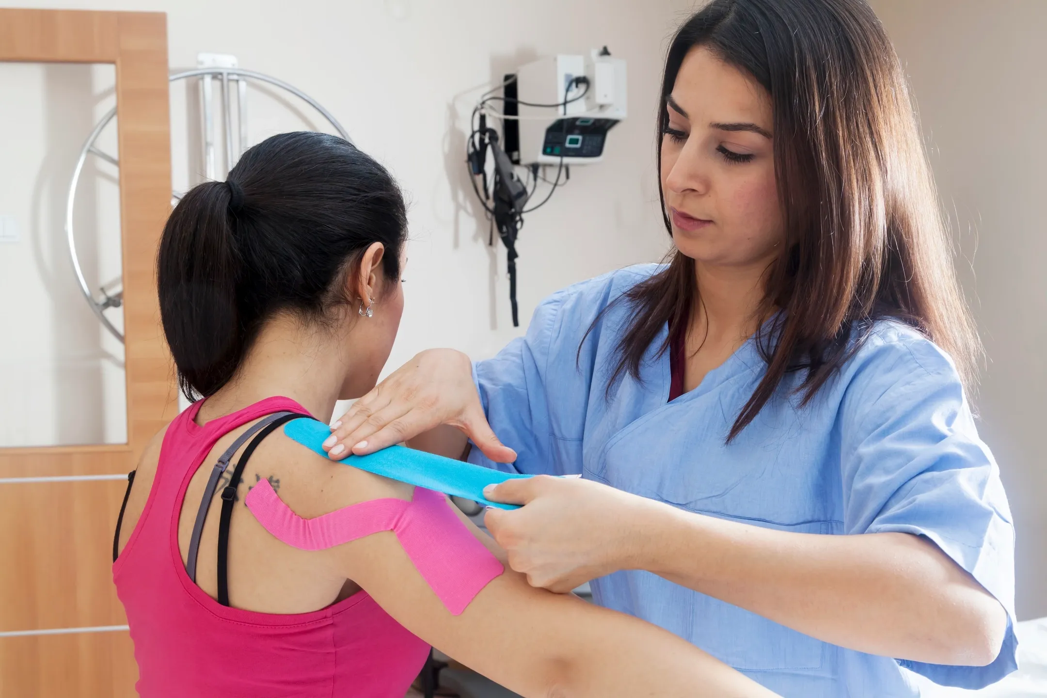 A woman is taping another person 's arm.