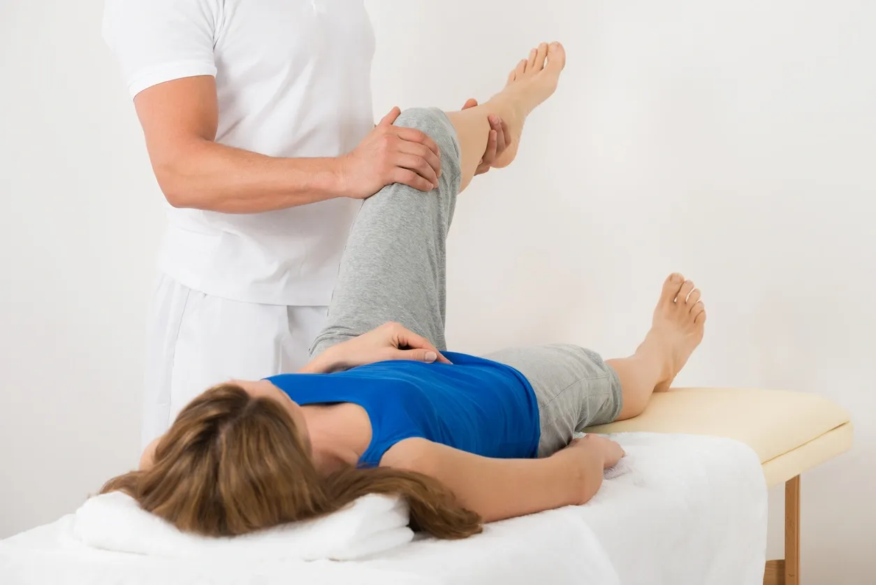 A woman is lying on the bed while another person stands over her.