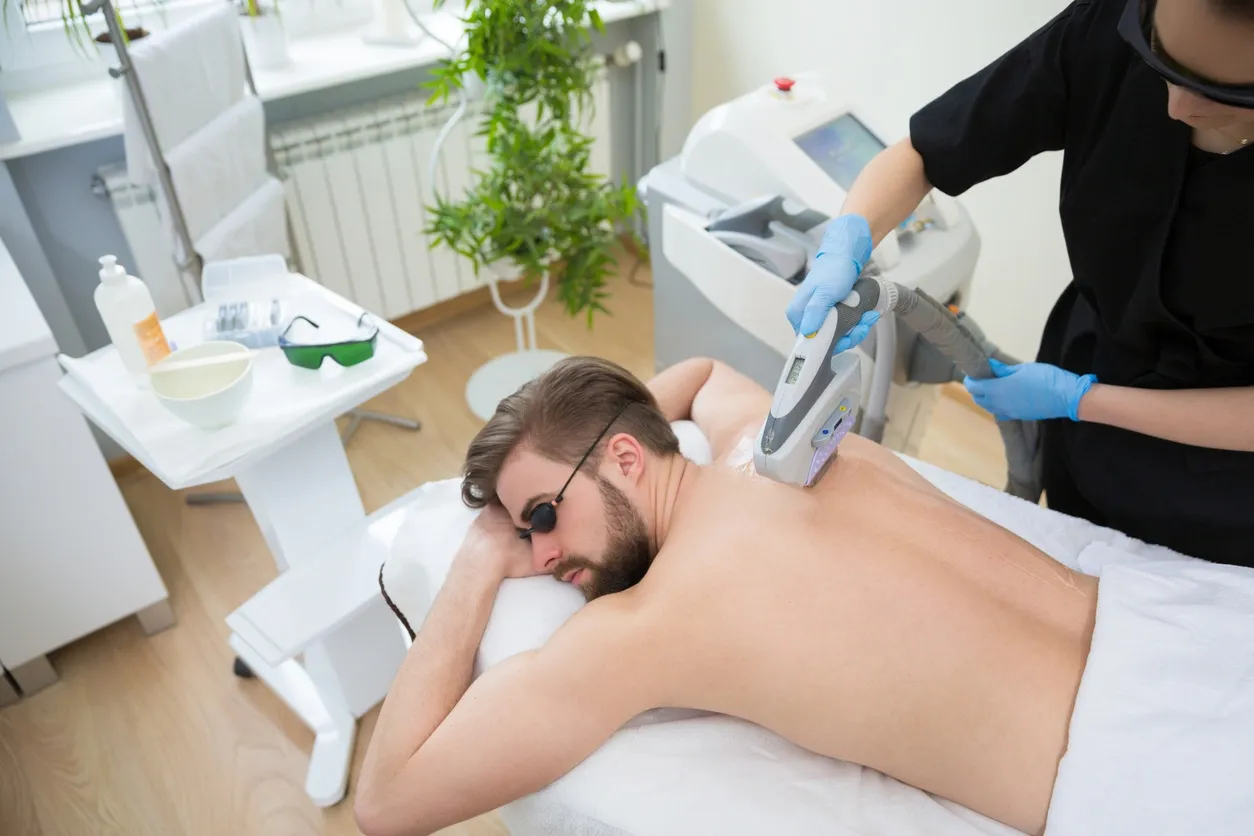 A man getting his back shaved and underarm hair removed.