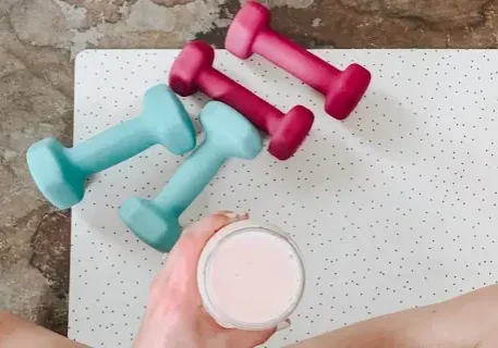 A person holding a cup of milk next to four dumbbells.