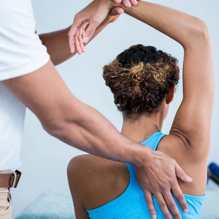 A person is stretching with another person touching her arm.