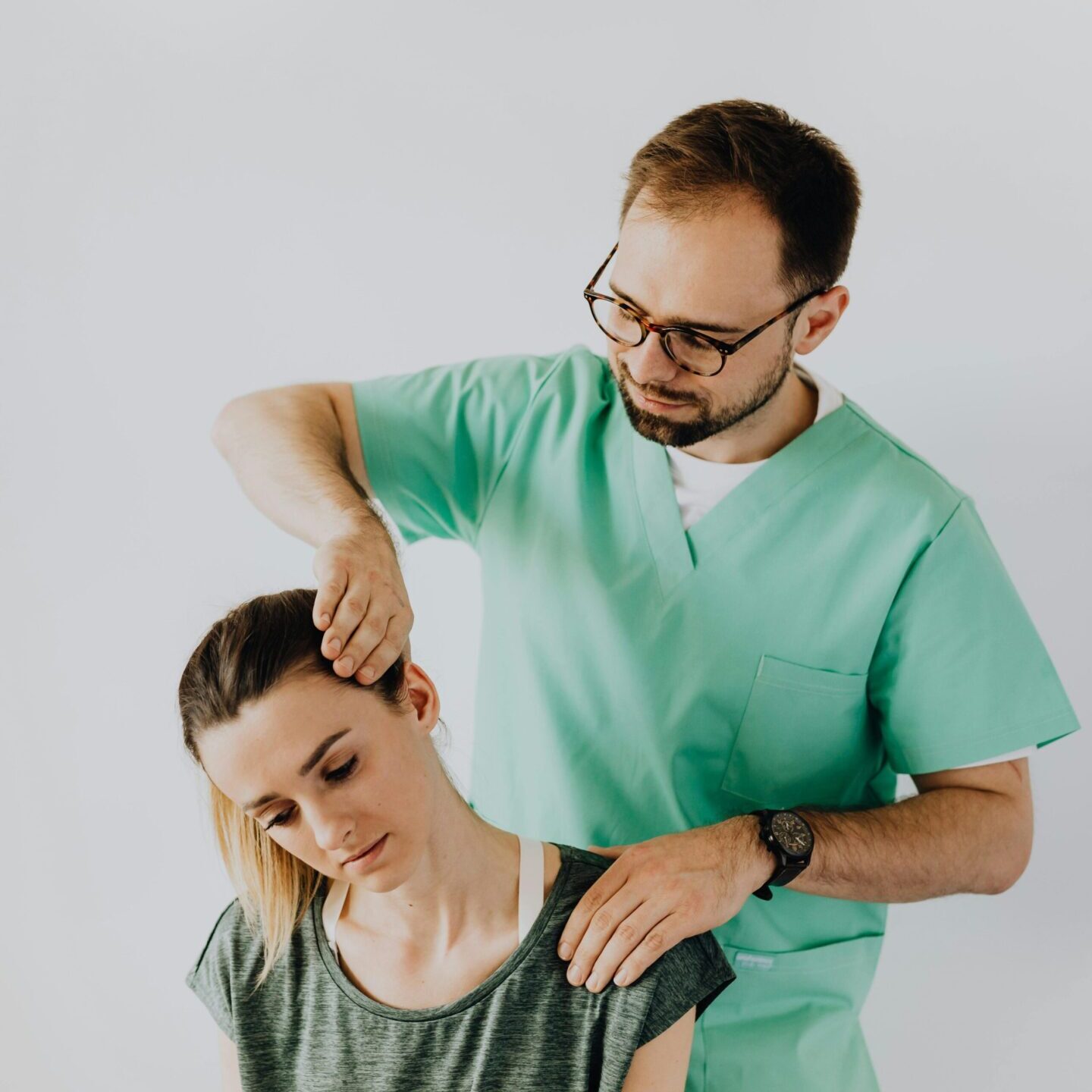 A man in green scrubs is combing the hair of another person.